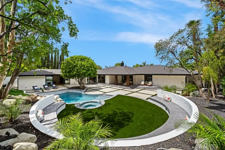 Landscaped backyard with a curved pool beside a single-story home