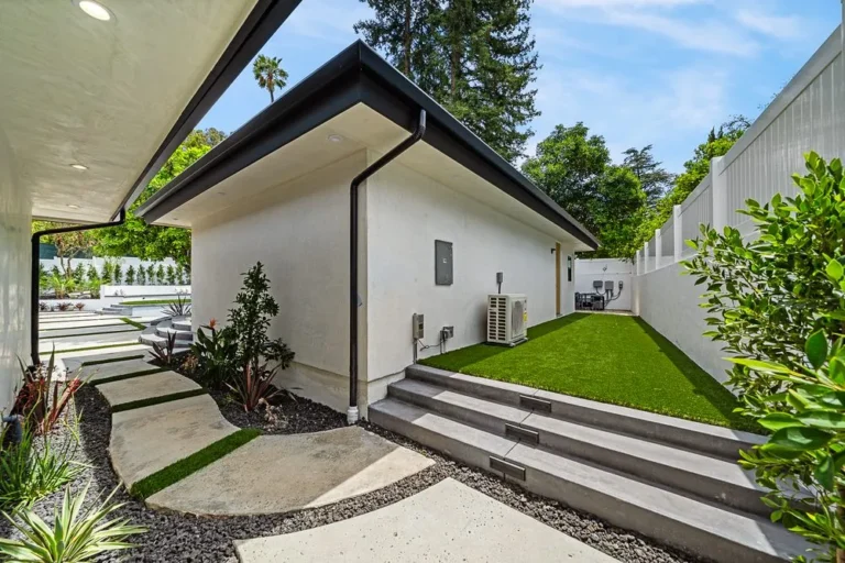 Side yard of a modern flat-roofed home with a paved walkway and step lighting